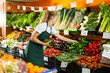 © JackF - Positive young female seller in uniform holding green pepper in grocery shop
