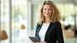 © Yusta Mizan - oung businesswoman holding an iPad, ready for success in a modern office setting.
