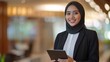 © Yusta Mizan - Confident young businesswoman holding a tablet, ready for success in a modern office setting
