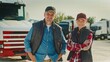 © VAKSMANV - Front camera view of Caucasian couple standing together in middle of parking lot. Truckers working in delivery company. Looking directly at camera while smiling. Lorries in blurred background.