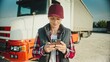 © VAKSMANV - Beautiful Caucasian woman standing next to her truck while using mobile phone. Typing on screen with fingers. Browsing social media or texting with friends online. Socializing remotely.