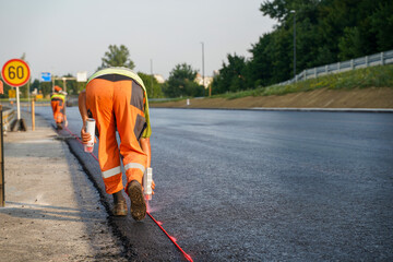 Fototapete - Construction Worker Marking Fresh Asphalt with Spray Can on Highway