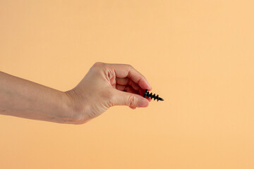 Wall Mural - A black screw in hand on cream background.

