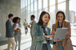 © Drazen - Happy businesswomen using laptop in hallway of office building.