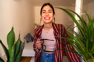 a joyful woman in casual attire smiling at the camera, surrounded by healthy indoor plants in a peac