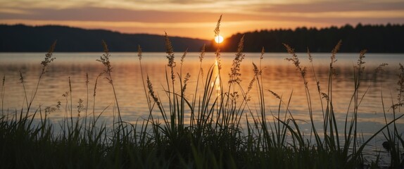 Wall Mural - Sunset over tranquil lake with grass silhouettes in foreground and reflection on water creating serene atmosphere Copy Space