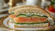 © fivan - A delicate close-up of a smoked salmon and cucumber tea sandwich with visible layers of salmon, cucumber, and herbed cream cheese, placed on a gold-rimmed plate