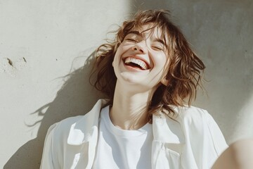 Wall Mural - Photo of a laughing woman wearing a white t-shirt and a white jacket, kicking her legs, on a gray background. Simple and feminine composition with a sunlight background, typical of stock photos.