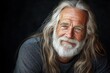 © ChaoticMind - Elderly man with long gray hair and beard poses warmly against a dark background in a relaxed and inviting manner