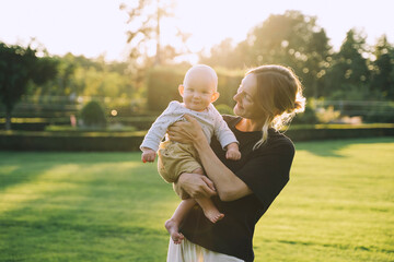 Wall Mural - Young mother and baby playing in park at summer. Beautiful mom and child outdoors. Parent with kid spend time together. Happy healthy family at sunlight. Eco sustainable lifestyle. Positive emotions.