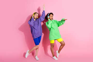 Canvas Print - Vibrant shot of two stylish young women dancing in sportswear hoodies demonstrating carefree friendship with pink backdrop