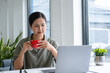© MIND AND I - Businesswoman sitting at desk on couch in workplace or at home working on laptop and analyzing data on charts and graphs and writing on papers to make business plan and strategies for company
