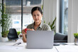 © MIND AND I - Businesswoman sitting at desk on couch in workplace or at home working on laptop and analyzing data on charts and graphs and writing on papers to make business plan and strategies for company