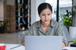 © MIND AND I - Businesswoman sitting at desk on couch in workplace or at home working on laptop and analyzing data on charts and graphs and writing on papers to make business plan and strategies for company