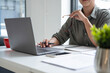 © MIND AND I - Businesswoman sitting at desk on couch in workplace or at home working on laptop and analyzing data on charts and graphs and writing on papers to make business plan and strategies for company