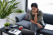© MIND AND I - Businesswoman sitting at desk on couch in workplace or at home working on laptop and analyzing data on charts and graphs and writing on papers to make business plan and strategies for company