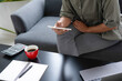 © MIND AND I - Businesswoman sitting at desk on couch in workplace or at home working on laptop and analyzing data on charts and graphs and writing on papers to make business plan and strategies for company