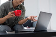 © MIND AND I - Businesswoman sitting at desk on couch in workplace or at home working on laptop and analyzing data on charts and graphs and writing on papers to make business plan and strategies for company