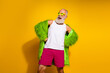 © deagreez - Charismatic senior man in vibrant retro outfit expressing freedom and style against a bold yellow background
