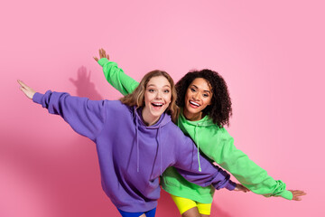 Canvas Print - Cheerful young women in vibrant hoodies posing playfully against a pink background, symbolizing friendship, youth, and style.