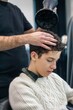 © Lomb - Professional hairstylist drying a young client’s hair at a barbershop. Close-up on the hands of the stylist using a blow dryer, emphasizing self-care, grooming, and beauty services.