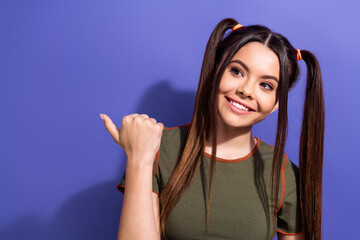 Wall Mural - Charming young woman with ponytails smiling brightly on a purple background with a casual and fashionable look