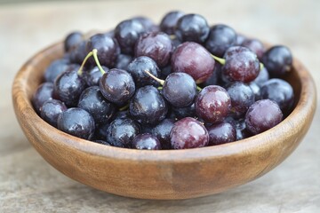 Poster - Freshly harvested dark grapes displayed in a rustic wooden bowl on a textured surface