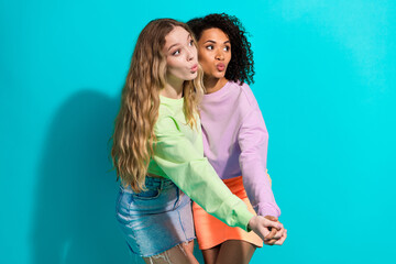 Wall Mural - Two fashionable young women enjoying vibrant turquoise background, expressing fun and friendship