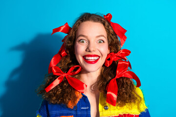 Wall Mural - Happy young woman with vibrant red ribbon in hair against a colorful blue background exuding cheerful expressions and trendy fashion.