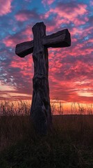 Wall Mural - Large wooden cross stands tall against the backdrop of an orange and blue sky at sunset, symbolizing Jesus' sacrifice for all people. 