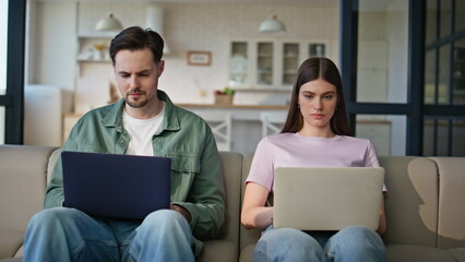 Wall Mural - Home sweethearts browsing laptops at soft couch place. Young couple working