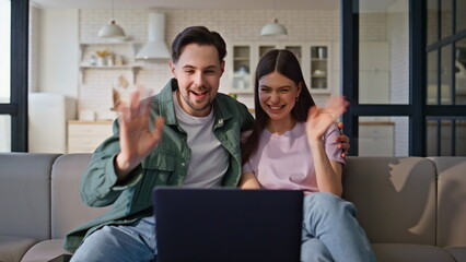 Wall Mural - Overjoyed pair making video conference greeting laptop emotionally. Fun couple