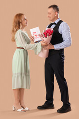 Wall Mural - Middle-aged couple with bouquet of flowers and greeting card on beige background. International Women's Day