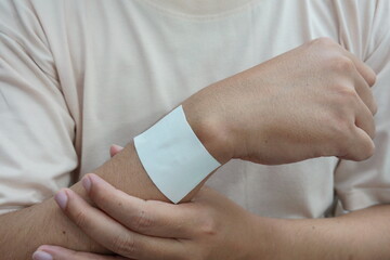 close up of a patient with a beige shirt wearing a white medicated patch on a hand for pain relief.