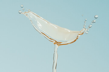 Poster - Liquid Art: A splash of amber liquid freezes in mid-air, forming an elegant and abstract shape against a soft blue background. The image evokes a sense of movement and fluidity.
