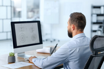 Technician making digital engineering drawing on computer at desk in office, back view