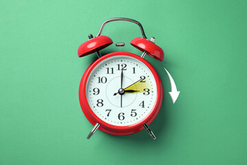 Poster - Daylight saving time. Red alarm clock on green background, top view. Highlighted area and arrow showing time change by one hour forward