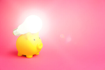 Wall Mural - Piggy bank and glowing light bulb on pink background, space for text. Energy saving concept