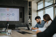 © qunica.com - Business people from diverse backgrounds collaborate in a modern office setting. They are focused on a presentation displayed on a large screen, analyzing data and strategies.
