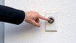 © agnes - A close-up of a professional hand in a suit pressing a white doorbell button representing access security and communication in business or home settings
