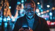 © Johannes - Smiling man using smart phone during night. Closeup face of happy mature businessman messaging on cellphone at night on the street with the lights of the road blurred in the background.