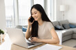 © fizkes - Asian woman sit at desk, smile, lead talk on smartphone, engaged in remote conversation, having phone call at home discussing work-related matters, receive help speaking to customer services manager