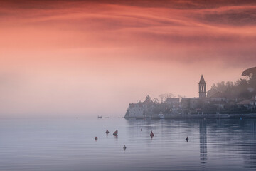 Wall Mural - Low lying fog covering small coastal town at sunrise with mountains in the background