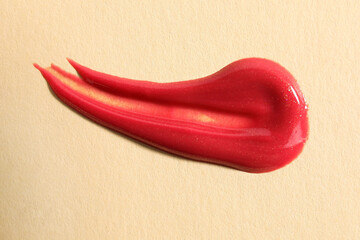 Wall Mural - Sample of red lipgloss on beige background, top view