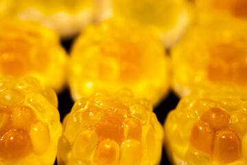 Wall Mural - An extreme close-up of a transparent, yellow gummy candy with a bumpy, textured surface resembling a fruit or honeycomb shape. The shiny details stand out against a dark background.
