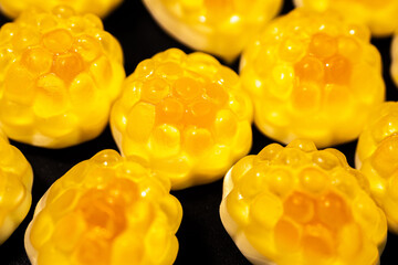 Wall Mural - An extreme close-up of a transparent, yellow gummy candy with a bumpy, textured surface resembling a fruit or honeycomb shape. The shiny details stand out against a dark background.
