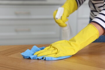 Wall Mural - Woman using cleaning product while wiping wooden table with rag indoors, closeup. Space for text