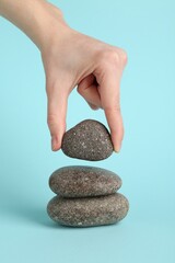 Wall Mural - Woman making stack of stones on light blue background, closeup. Harmony and life balance