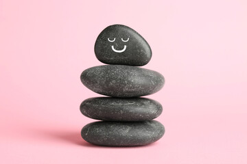 Wall Mural - Stack of rocks with drawn smiley face on light pink background. Harmony and life balance