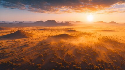 Wall Mural - Aerial view of sunrise over a vast, misty savanna landscape with rolling hills and scattered trees.